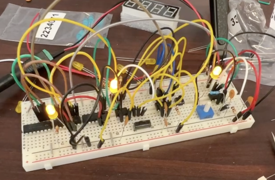 A photo of a breadboard with wires connecting between chips. There are three yellow lights.