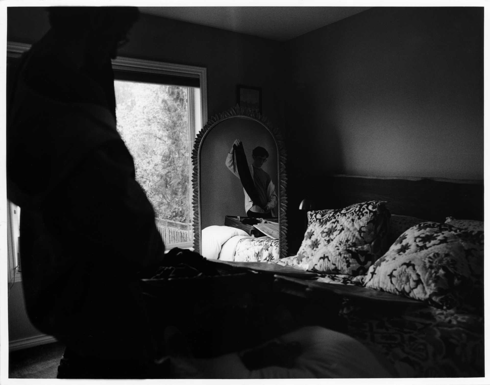 Black and white photo of me packing clothes into a suitcase. A large mirror is in the center of the frame reflecting me doing this.