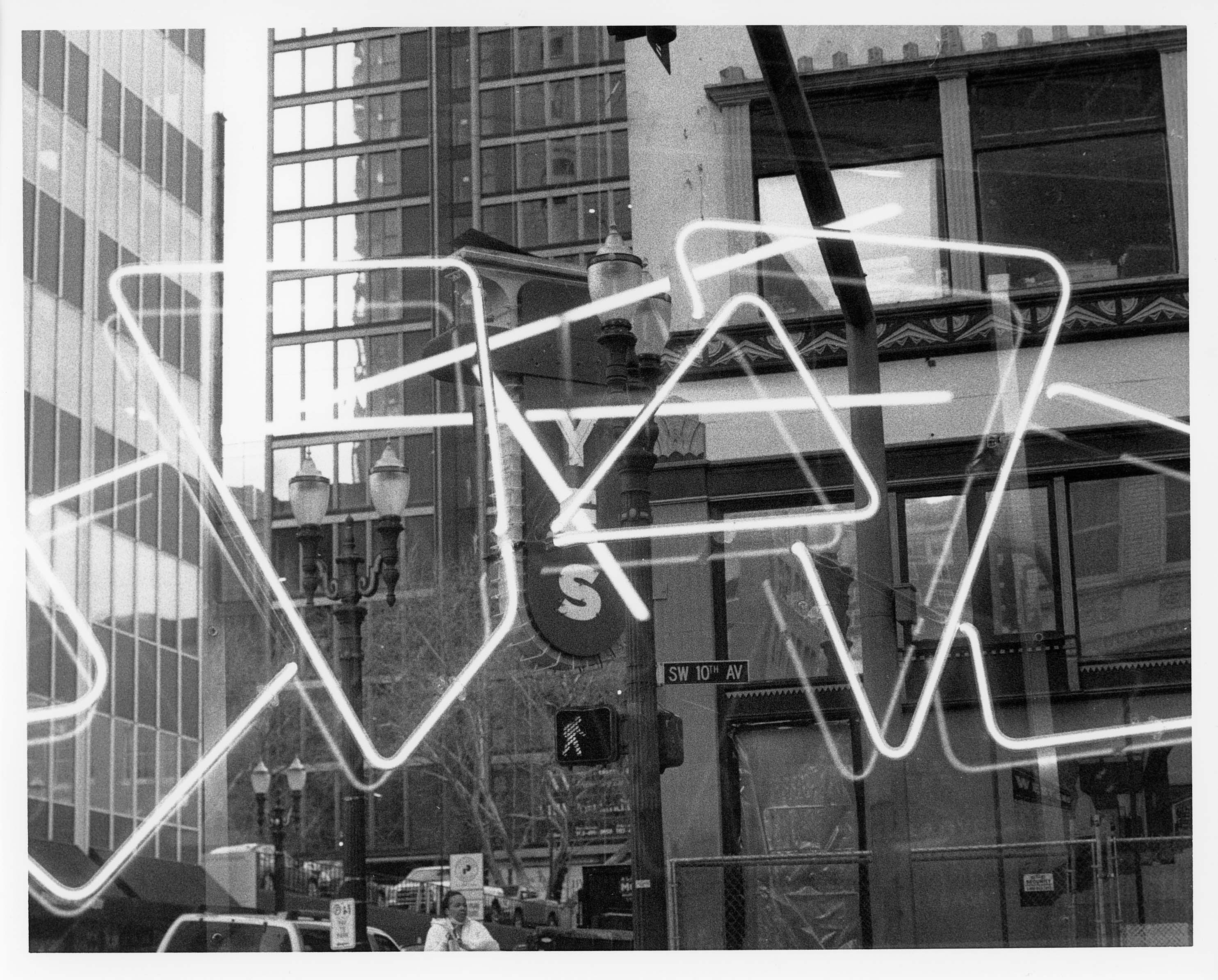 Black and white photo of neon light shapes in front of a cityscape.