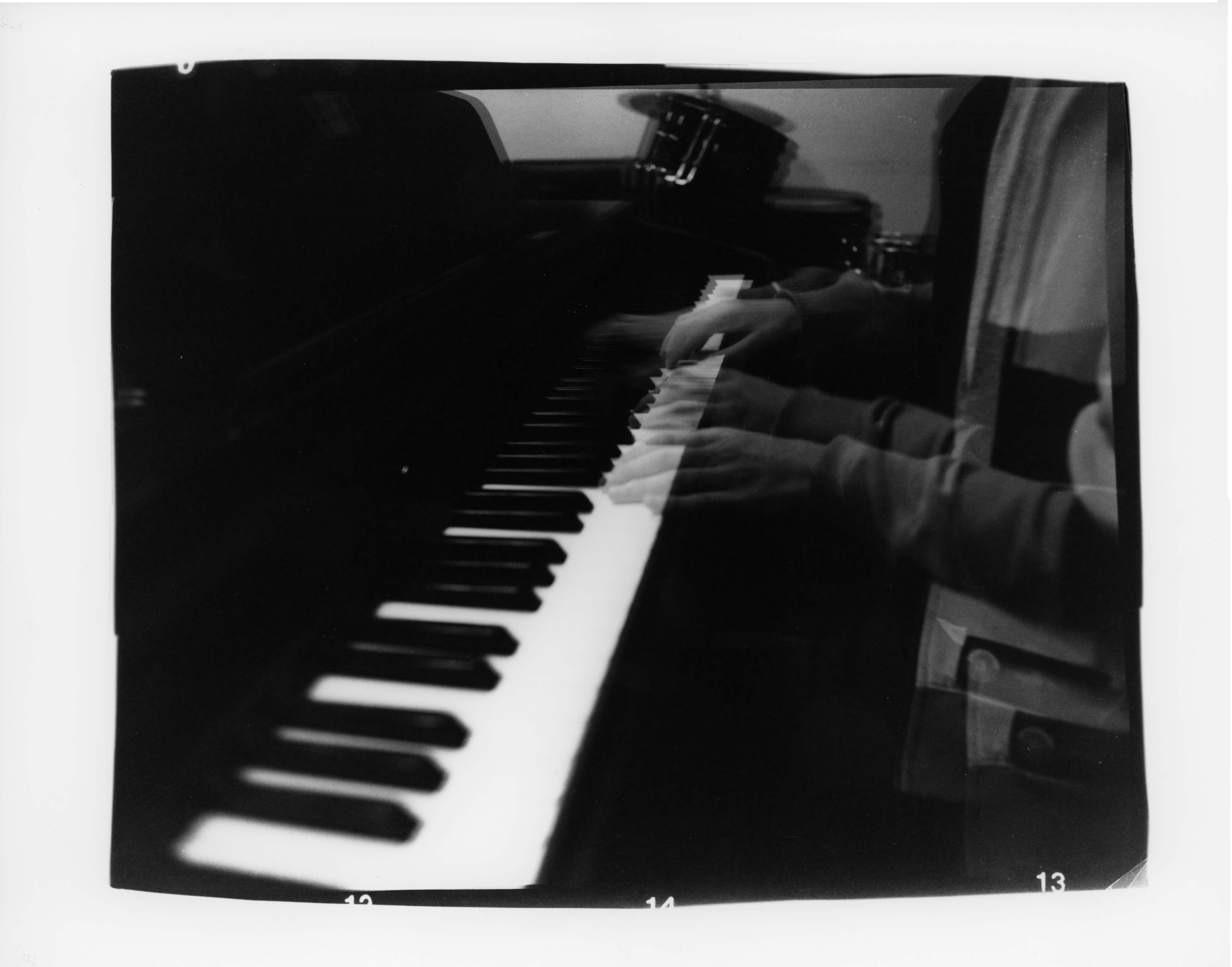 Black and white double exposure of someone playing the piano. They appear to have four hands.